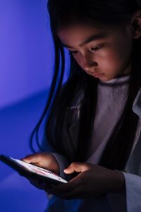 A child engrossed in a smartphone in a dimly lit room, highlighting technology use.